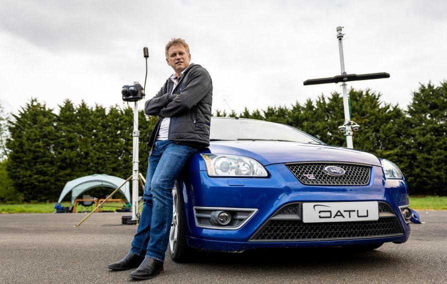 U.K. Secretary of State for Transport Grant Shapps sitting on blue car on test track